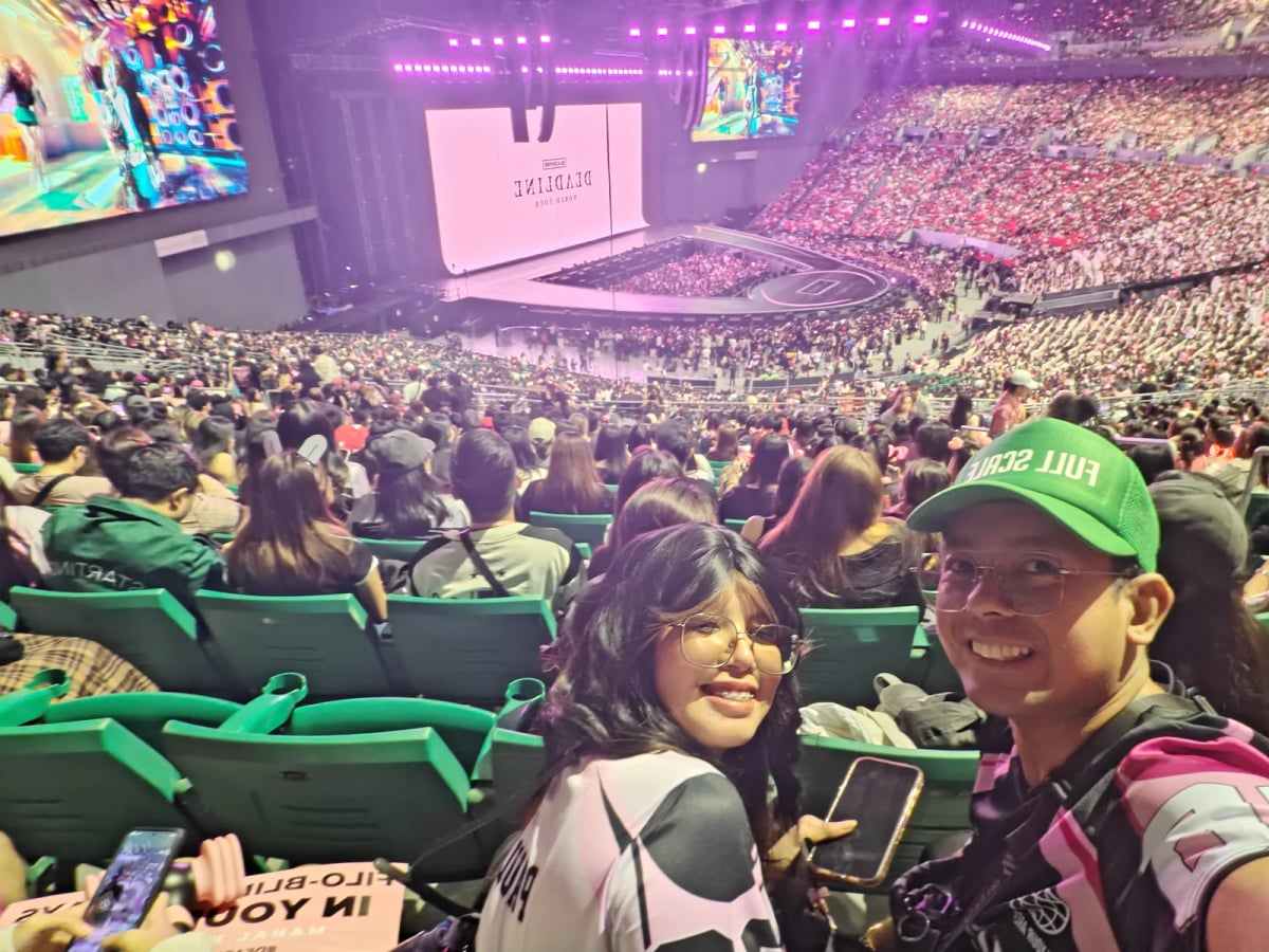 Two Full Scale employees, one wearing a green Full Scale cap, at the BLACKPINK concert with the packed Philippine Arena behind them